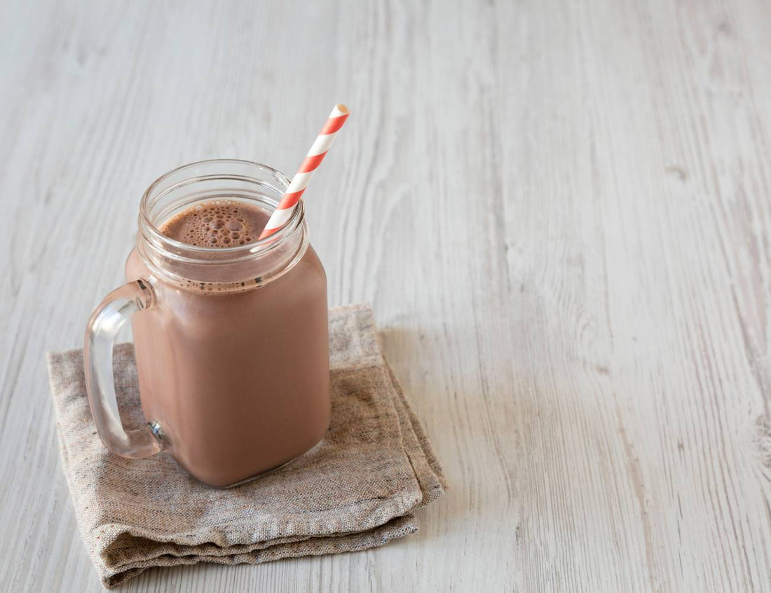 Glass mug with chocolate smoothie and red and white striped straw. On wooden background. 
