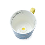 Sky-blue mug with dragonfly and daisy illustrations, yellow handle and interior, and ‘Live on tea and flowers’ message inside.