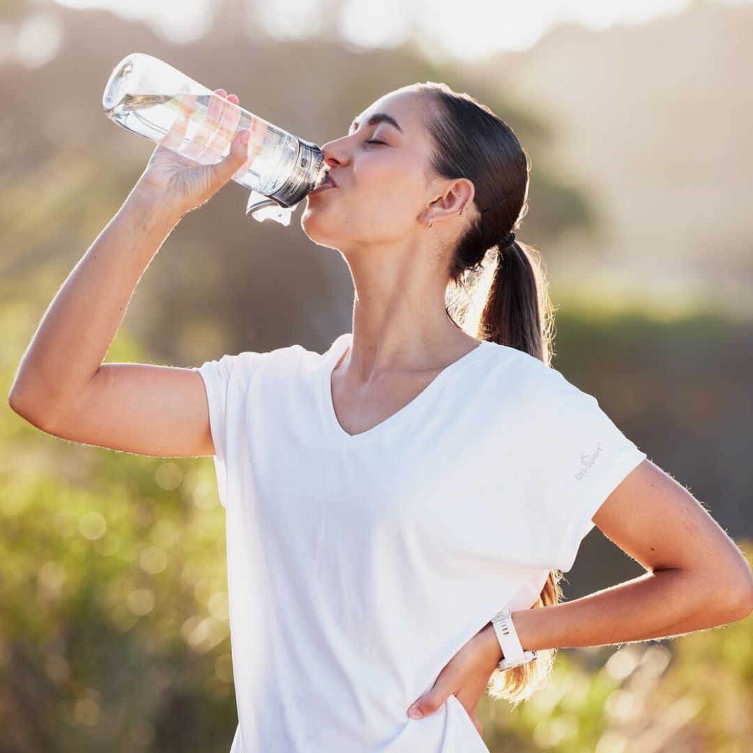 Woman drinking water outdoors with a blurred natural background